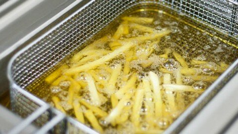 Frying French fries in cooking oil in kitchen