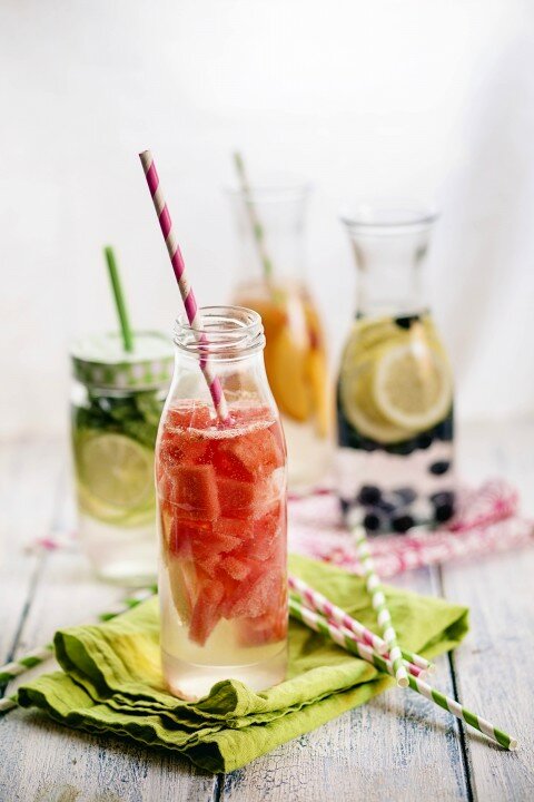 Carafes of miscellaneous fruit infused water on cloth and wood